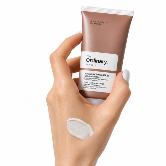 A hand holding The Ordinary Mineral UV Filters SPF 30 with Antioxidants sunscreen tube, with a small amount of white sunscreen cream applied to the back of the hand. The mineral-based SPF 30 formula provides broad-spectrum UVA/UVB protection while helping support skin hydration and antioxidant defense.