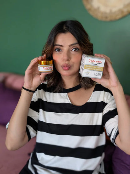 Woman holding two skincare products against a green wall.