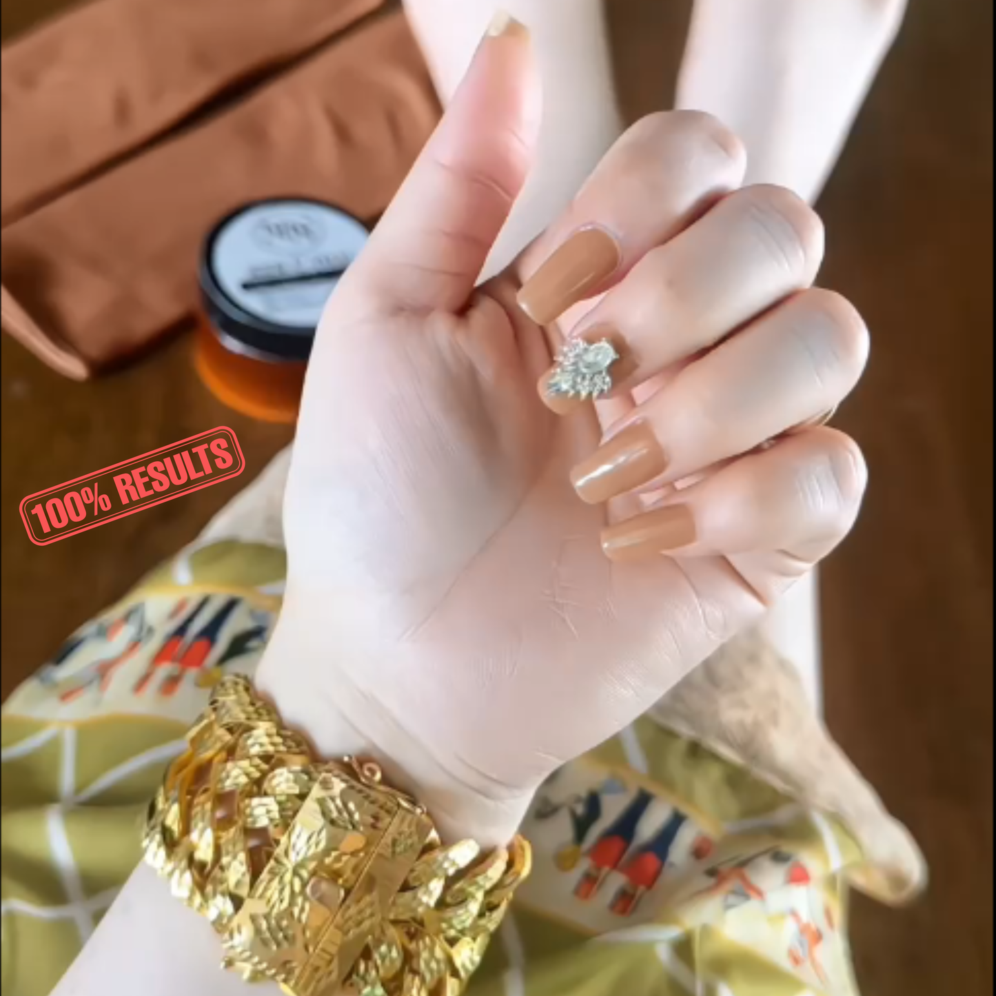 Hand wearing a gold bracelet with a small ring, against a blurred background.