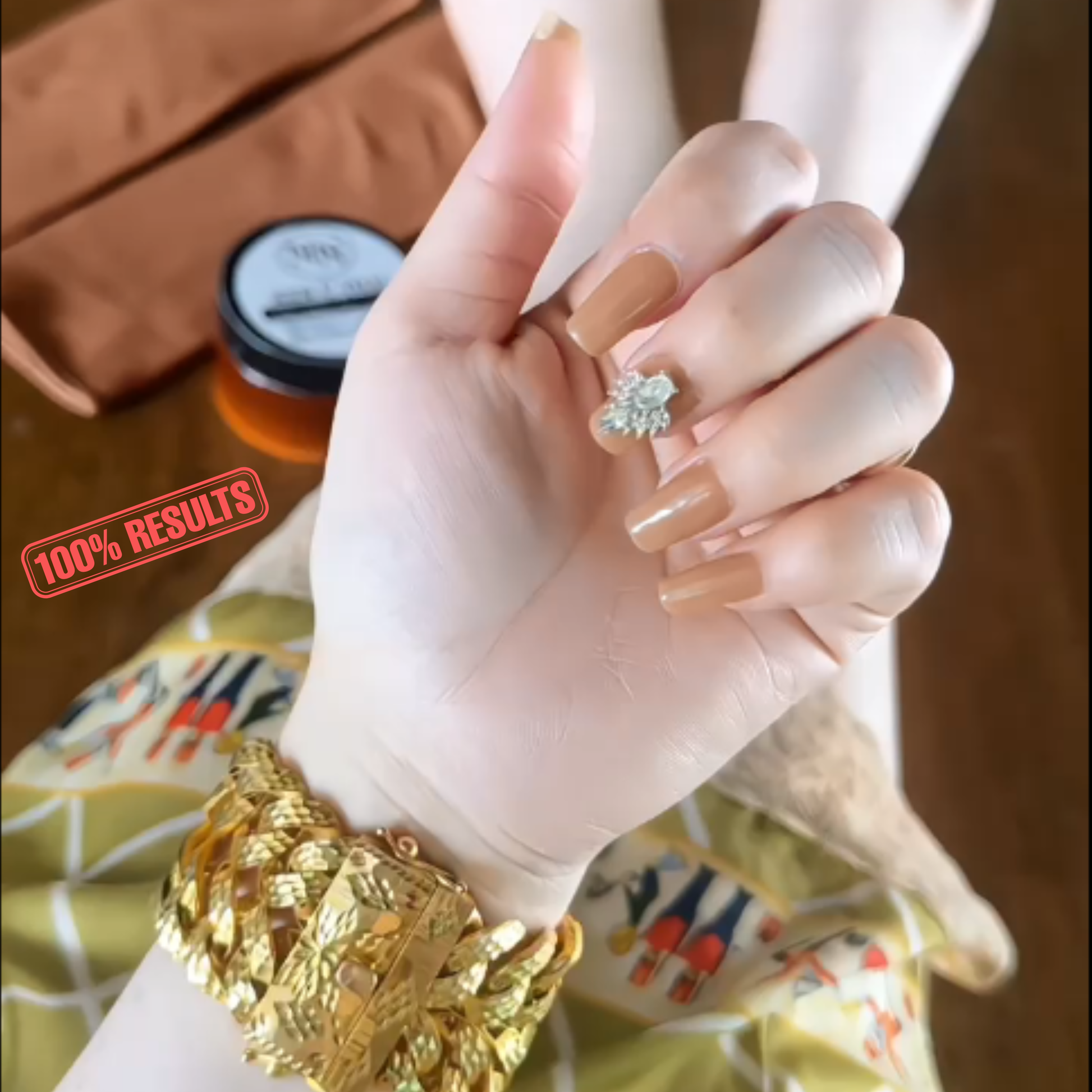 Hand wearing a gold bracelet with a small ring, against a blurred background.