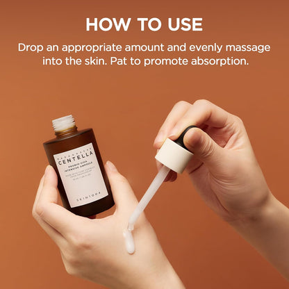 Demonstration of how to use SKIN1004 Madagascar Centella Probio-Cica Intensive Ampoule. A dropper dispenses the milky serum onto the back of a hand from the amber glass bottle. Instructions recommend applying an appropriate amount, gently massaging into the skin, and patting for better absorption to nourish, soothe, and strengthen the skin barrier.