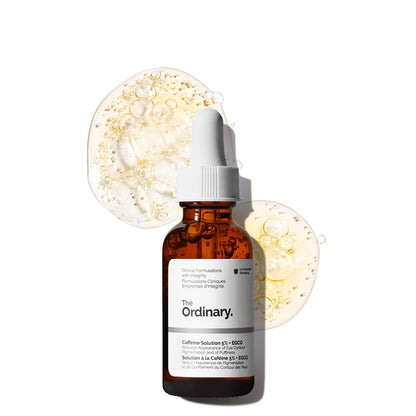 Amber glass bottle of The Ordinary Caffeine Solution 5% + EGCG eye serum with a white dropper cap, displayed against a light background with translucent serum textures. The depuffing eye serum is formulated to help reduce the appearance of dark circles, puffiness, and tired-looking eyes.