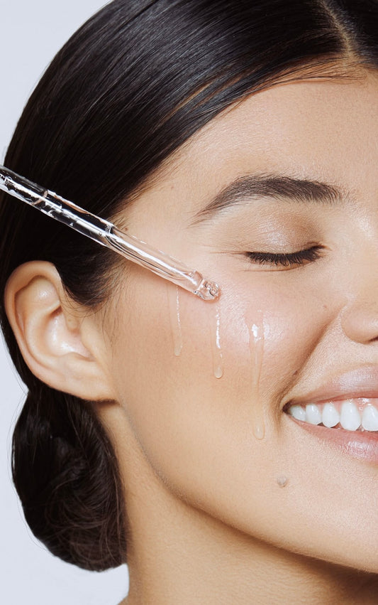 Woman applying a dropper of skincare product to her face.